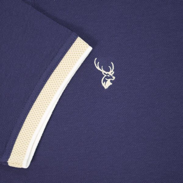 Navy blue polo shirt with beige trim and a white embroidered logo on a dark background